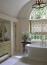 38 - Sissy Yellen, Elegant bathroom design Freestanding bathtub, Gold bathroom fixtures, Large arched window, Floral Roman shades, Soft natural lighting, Classic and timeless decor, Custom cabinetry
