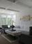 40 - Sissy Yellen, Bright living room design featuring modern traditional decor with coffered ceiling details, large picture windows, plush upholstered furniture in neutral tones, a tufted ottoman coffee table, and gold wall sconces providing an elegant touch to the space