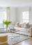 43 - Sissy Yellen, Bright modern living room featuring a light and airy interior with a neutral sofa, striped accent pillows, a glass and chrome coffee table, a yellow upholstered ottoman, and a cozy textured area rug, illuminated by natural light from large windows.